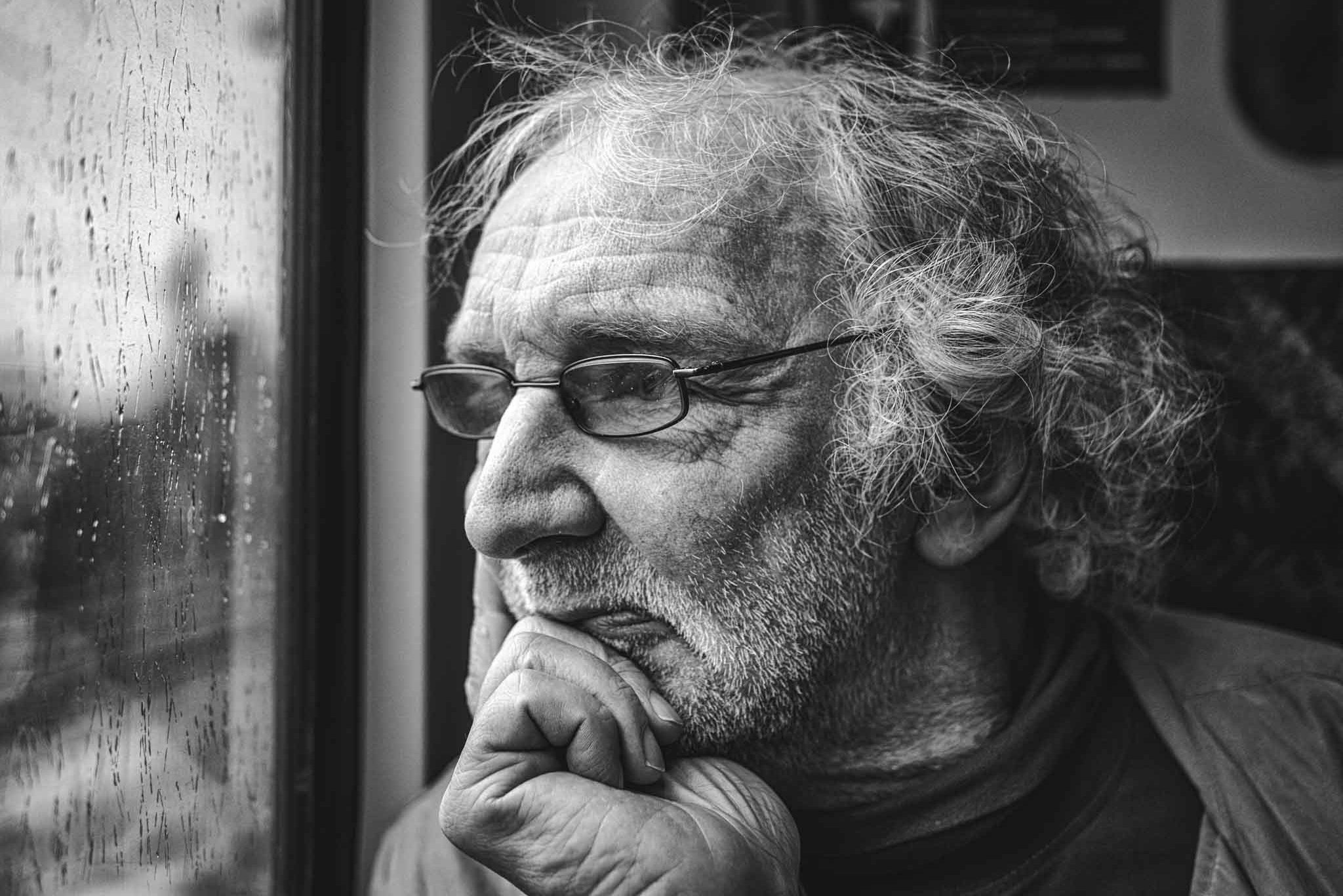 Porträt von einem alten Mann im Zug. Er hat den Kopf auf eine Hand gestützt und schaut aus dem Fenster. Man sieht ihm sein Leben an den Falten in Gesicht und Hand an.